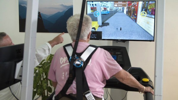 A physical therapist instructs an elderly patient on a VR treadmill using GaitBetter's virtual reality motor-cognitive intervention for gait training and preventing elderly falls
