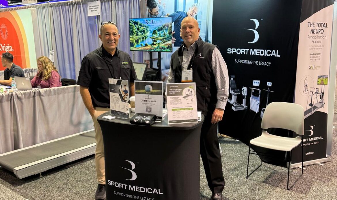 Two men standing at an exhibition booth, they are smiling at the camera. The booth has branded signage for Sport Medical, and GaitBetter. There is a treadmill with GaitBetter on the TV screen next to the treadmill.
